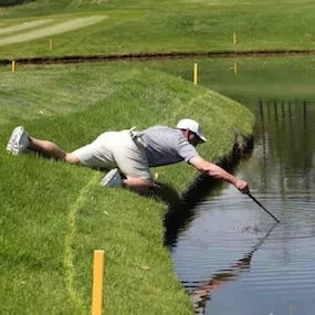 High handicap golfer pulling ball out of pond.