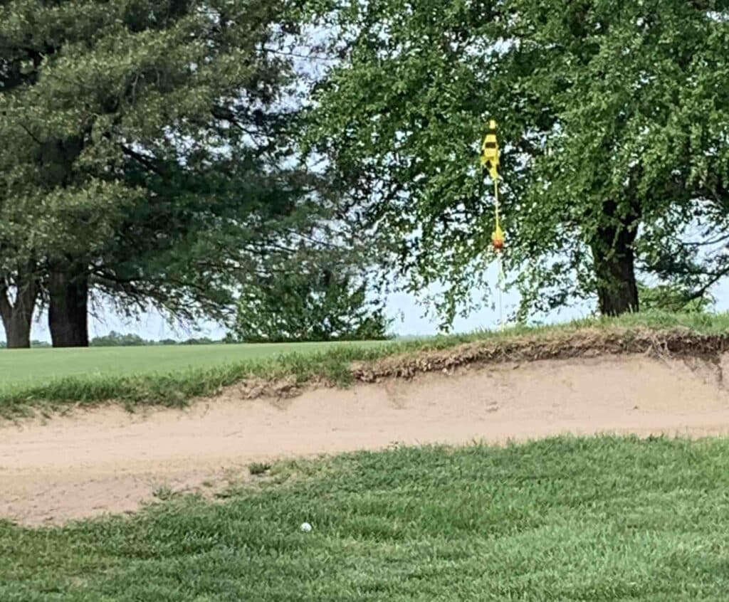 Ball next to a sand trap with the green just behind it.