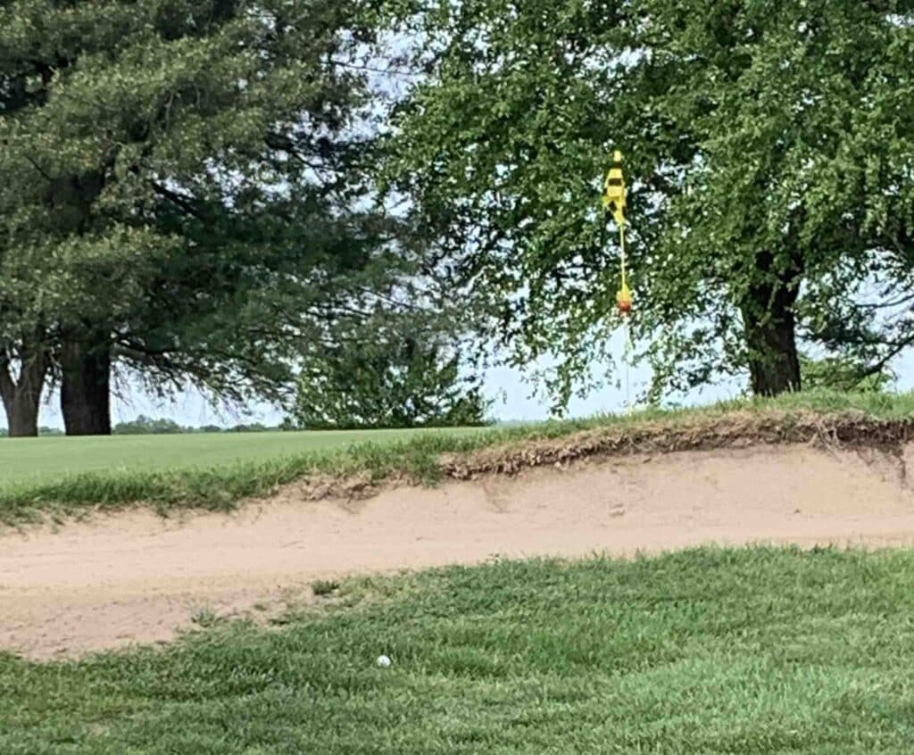 Ball next to a sand trap with the green just behind it. 