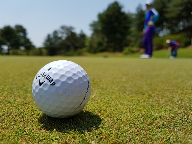 Golf ball on green grass with golf club in background