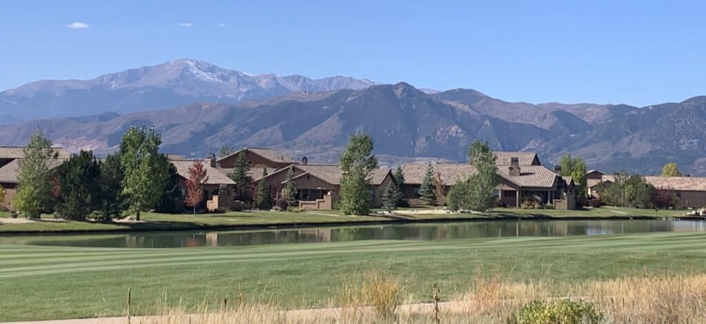 A scenic golf course, showing a fairway next to a pond.  On the other side of the pond are houses with beautiful mountains in the background.