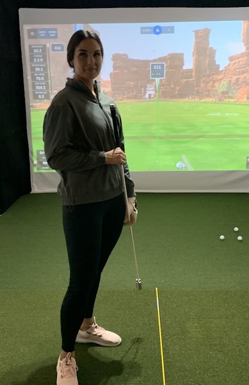 Golfer holding the Rypstick in front of a golf simulator.