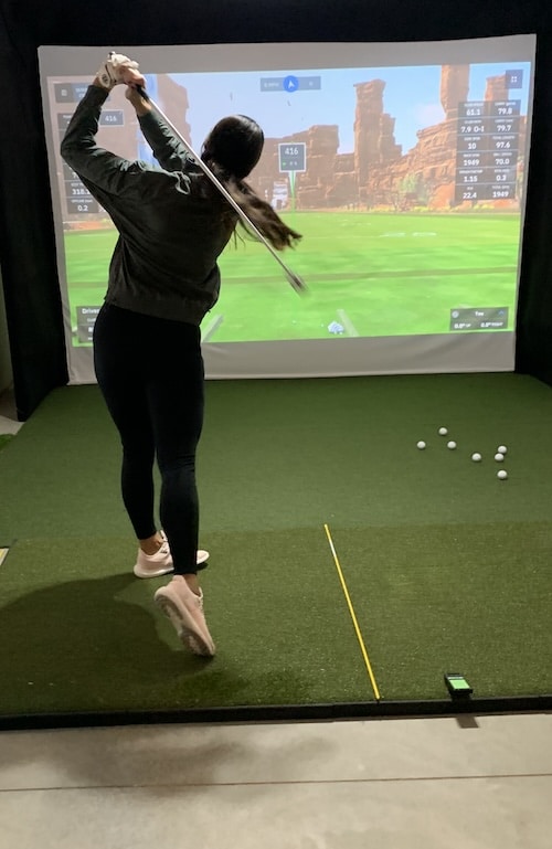 Golfer swinging the rypstick in front of a golf simulator