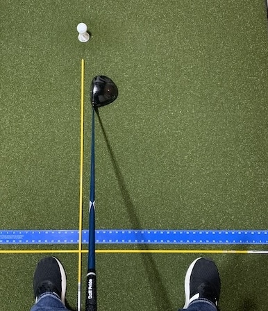 Golfer standing with a driver and alignment sticks displaying proper ball position aligned with the inside of the front foot.