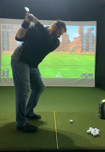 Tyler swinging a golf club in the simulator with the Prosendr wrist cradle