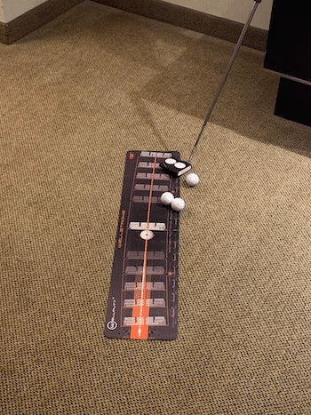 wellstroke mat with golf balls and a putter sitting in a hotel room